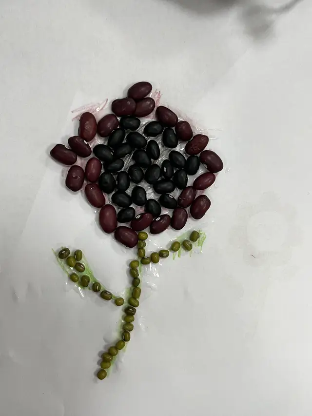 A flower made of glued red and black beans, with a stem of green mung beans