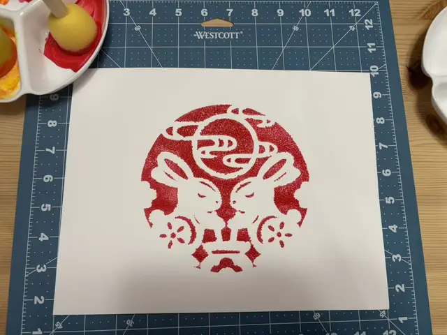 A red sponge-stencil print of two rabbits beneath a full moon, a Mid-Autumn Festival motif