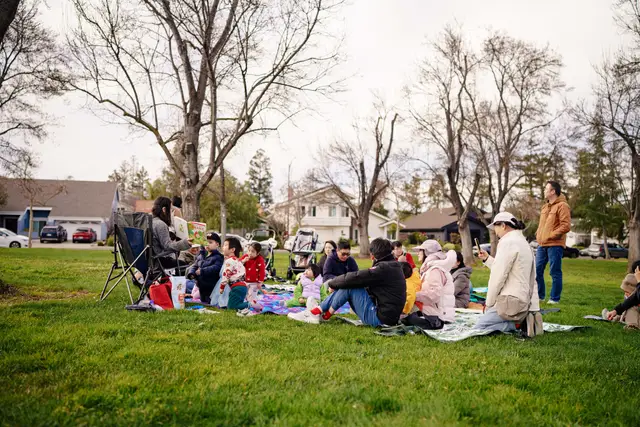Families seated on blankets under trees at a Bay Area reading club gathering