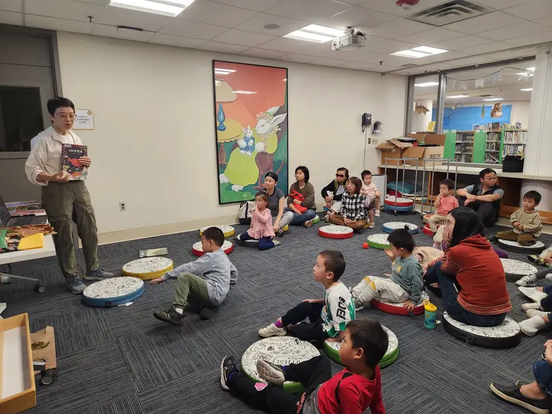 A volunteer reads aloud to children seated on floor cushions in a public library